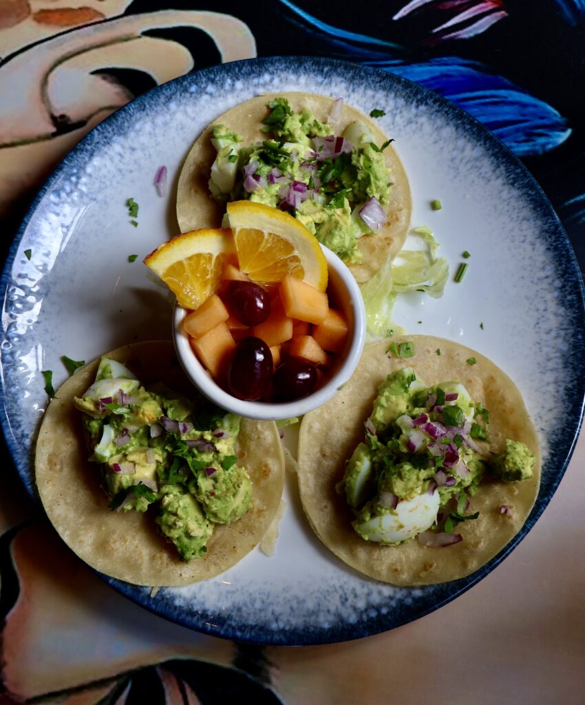 Breakfast tacos from Alero in Dupont Circle, Washington, DC, filled with scrambled eggs, cheese, avocado, and salsa, served with lime wedges on a white plate.